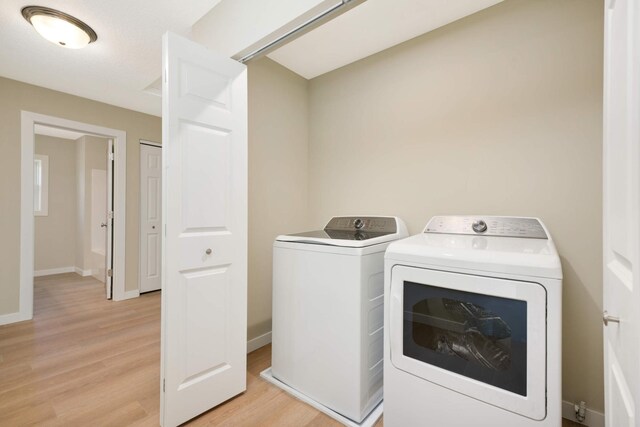 clothes washing area with independent washer and dryer and light wood-type flooring