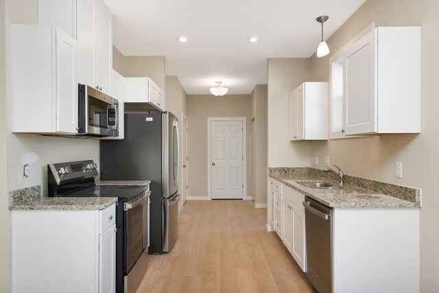 kitchen featuring stainless steel appliances, sink, decorative light fixtures, white cabinetry, and light hardwood / wood-style floors