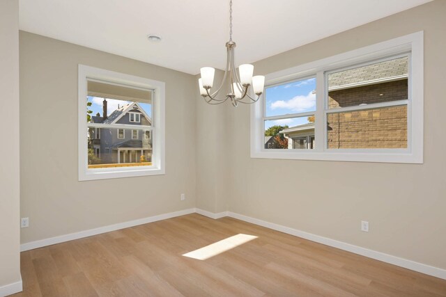 unfurnished room with light hardwood / wood-style floors, a healthy amount of sunlight, and a chandelier