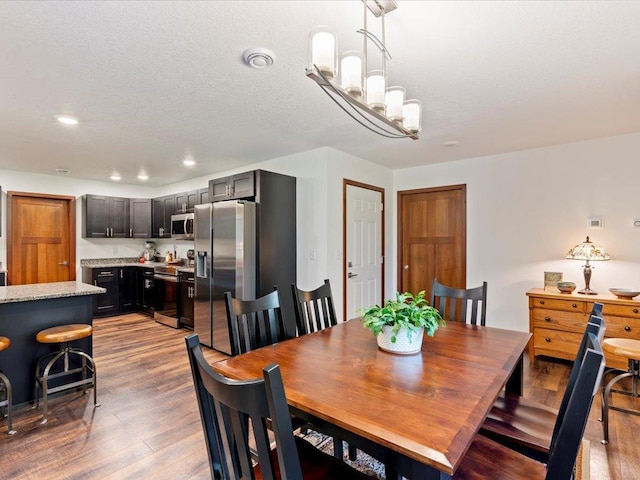 dining space with visible vents, wood finished floors, a textured ceiling, a notable chandelier, and recessed lighting