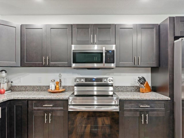 kitchen with stainless steel appliances, dark brown cabinets, and light stone countertops