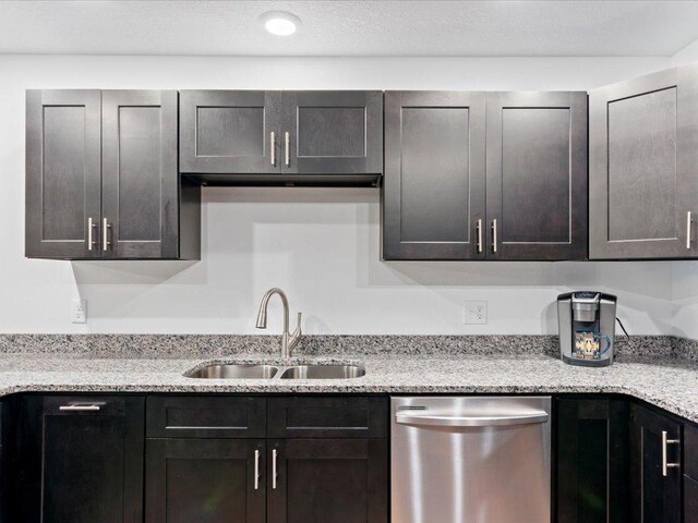 kitchen featuring dark brown cabinets, dishwasher, a sink, and light stone countertops