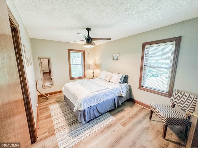 bedroom featuring a textured ceiling, light hardwood / wood-style flooring, ceiling fan, and multiple windows