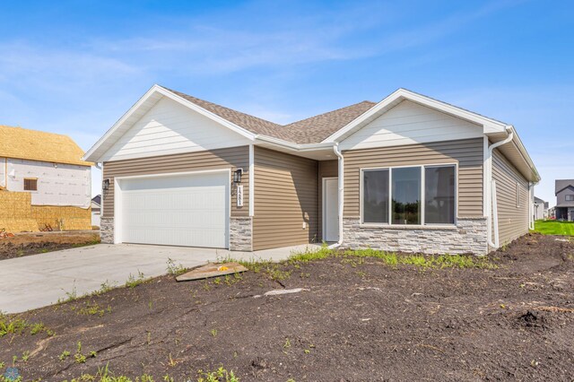 view of front facade with an attached garage, stone siding, driveway, and roof with shingles