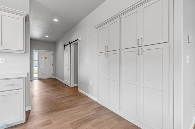 hall featuring light wood-style floors, a barn door, baseboards, and recessed lighting