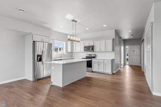 kitchen featuring stainless steel appliances, recessed lighting, light countertops, a kitchen island, and wood finished floors