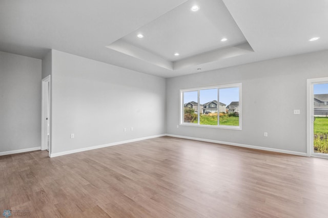 empty room with light wood-type flooring, a tray ceiling, baseboards, and recessed lighting