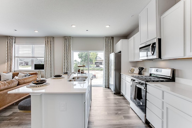 kitchen with stainless steel appliances, white cabinetry, sink, light wood-type flooring, and a kitchen island with sink