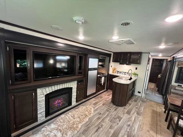 interior space with sink, a kitchen island, light hardwood / wood-style flooring, a stone fireplace, and crown molding