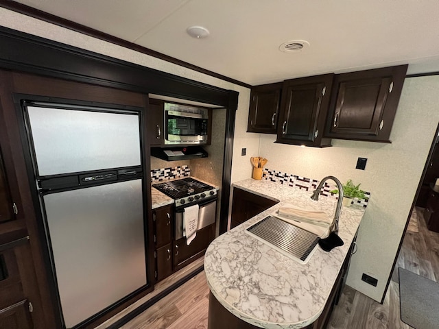 kitchen featuring visible vents, a peninsula, light wood finished floors, stainless steel appliances, and tasteful backsplash