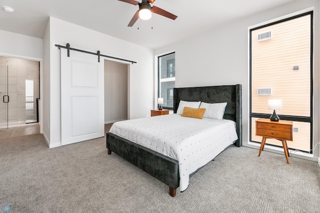 bedroom featuring ceiling fan, light colored carpet, a barn door, and ensuite bath