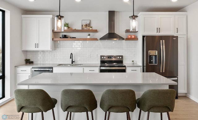 kitchen with appliances with stainless steel finishes, decorative light fixtures, sink, white cabinets, and wall chimney range hood