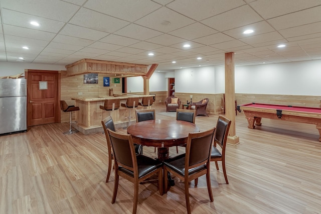 dining space with light wood-type flooring, indoor bar, wood walls, and billiards