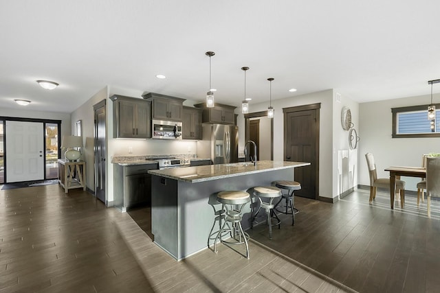 kitchen featuring appliances with stainless steel finishes, stone countertops, an island with sink, dark wood-type flooring, and a kitchen breakfast bar