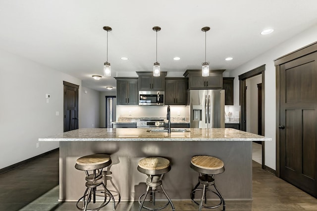 kitchen featuring a kitchen island with sink, decorative light fixtures, stainless steel appliances, a breakfast bar, and dark wood-type flooring