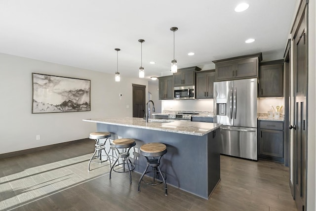 kitchen with an island with sink, stainless steel appliances, light stone countertops, and dark hardwood / wood-style flooring