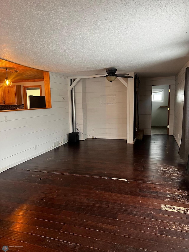 unfurnished living room with dark hardwood / wood-style floors, a textured ceiling, and wooden walls