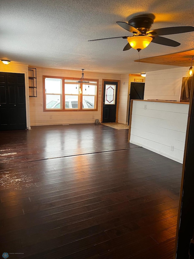 unfurnished living room with ceiling fan, dark hardwood / wood-style flooring, a textured ceiling, and wooden walls