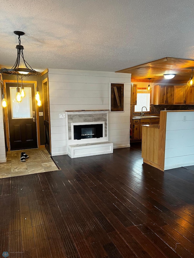 unfurnished living room with a textured ceiling, wooden walls, sink, and dark hardwood / wood-style floors