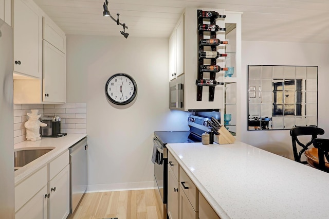 kitchen with tasteful backsplash, light hardwood / wood-style flooring, appliances with stainless steel finishes, track lighting, and white cabinets