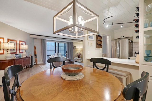 dining space featuring light hardwood / wood-style floors, baseboard heating, track lighting, and a notable chandelier