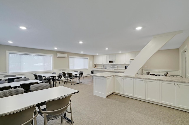 kitchen with white cabinetry, light stone counters, an AC wall unit, and sink