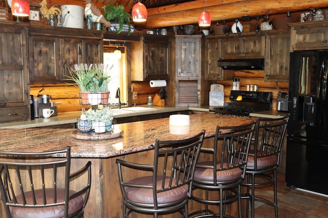 kitchen with hanging light fixtures, sink, black appliances, ventilation hood, and light stone countertops