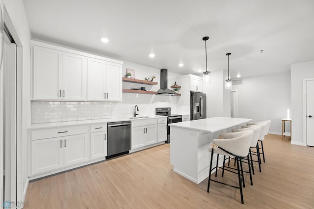 kitchen with pendant lighting, sink, appliances with stainless steel finishes, white cabinets, and wall chimney exhaust hood