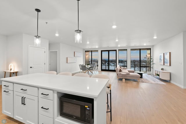 kitchen featuring pendant lighting, white cabinetry, expansive windows, a center island, and light wood-type flooring