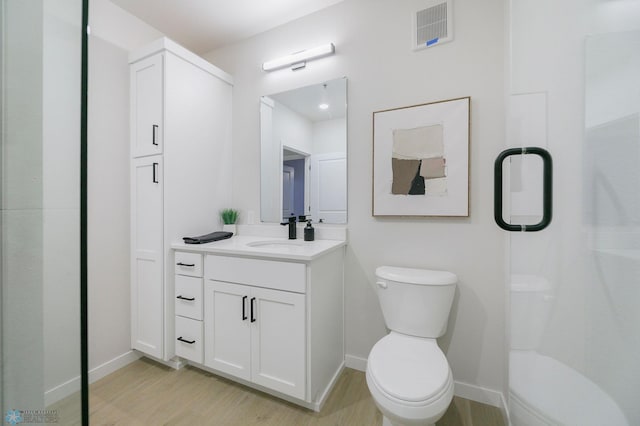 bathroom featuring vanity, wood-type flooring, a shower with shower door, and toilet