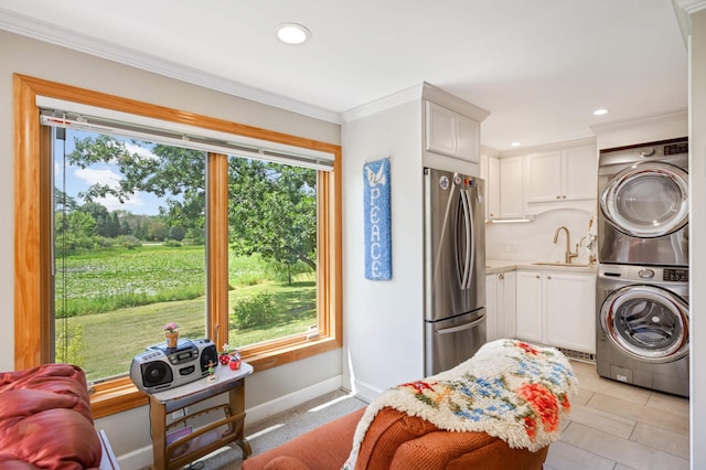 clothes washing area featuring sink, stacked washer / drying machine, light tile patterned floors, and ornamental molding