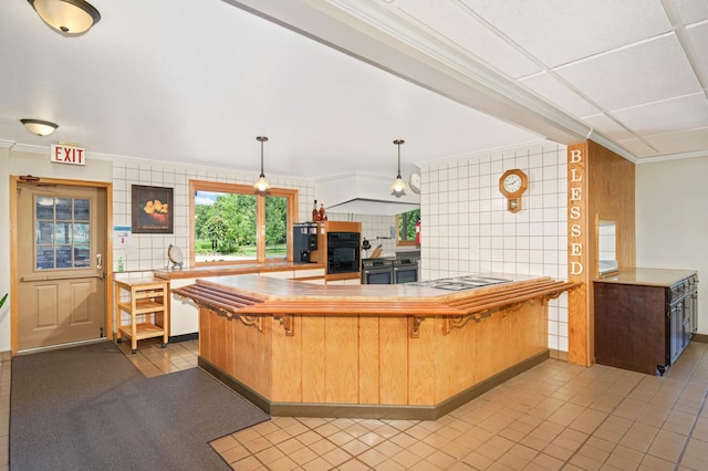 kitchen with kitchen peninsula, black appliances, tile patterned floors, a kitchen breakfast bar, and tile walls