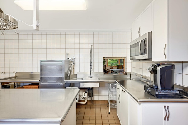 kitchen featuring white cabinets, light tile patterned flooring, stainless steel counters, and decorative backsplash