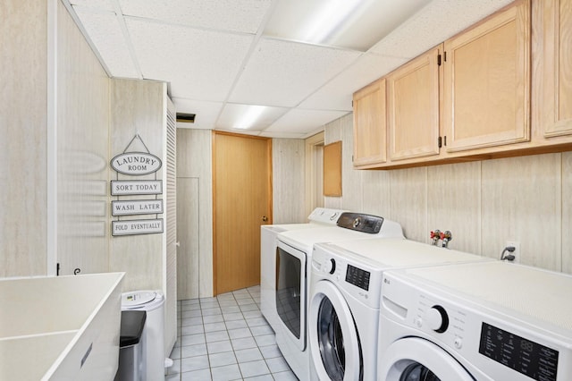 laundry area with wood walls, washer and clothes dryer, light tile patterned floors, and cabinets