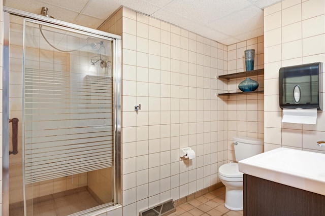 bathroom featuring a paneled ceiling, toilet, vanity, tile walls, and tile patterned floors