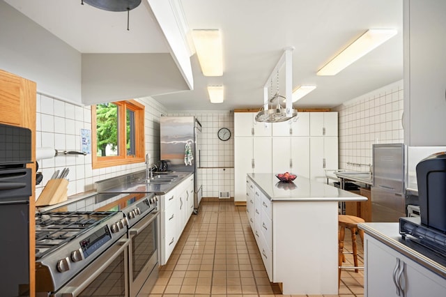 kitchen featuring tasteful backsplash, high end range, white cabinets, light tile patterned floors, and a kitchen island