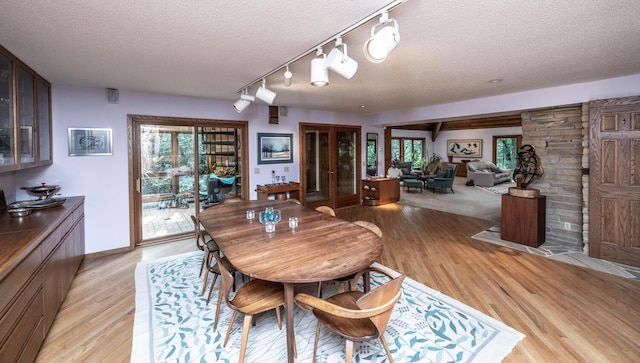 dining space with a textured ceiling, rail lighting, french doors, and light wood-type flooring