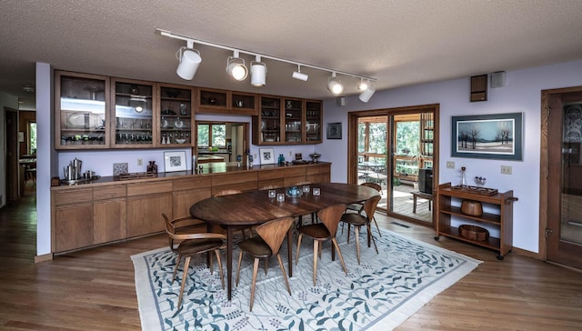 dining area with a textured ceiling, dark wood-type flooring, and bar