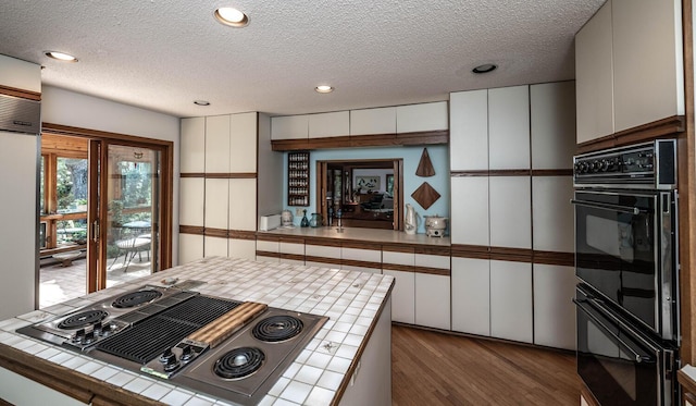 kitchen featuring stainless steel gas stovetop, tile counters, a textured ceiling, double oven, and white cabinets