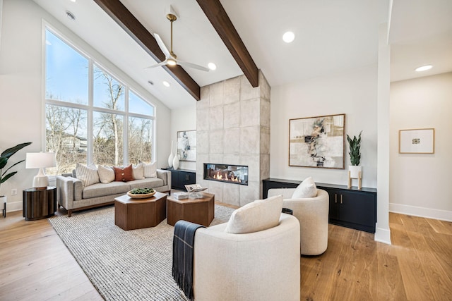 living room with light hardwood / wood-style floors, beamed ceiling, high vaulted ceiling, a tile fireplace, and ceiling fan