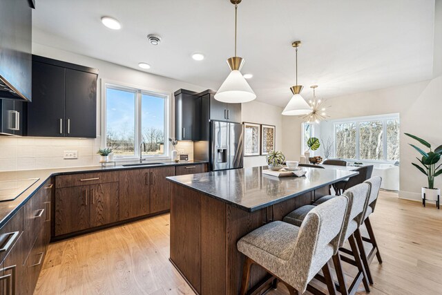 kitchen with stainless steel fridge with ice dispenser, backsplash, light hardwood / wood-style floors, and a kitchen breakfast bar