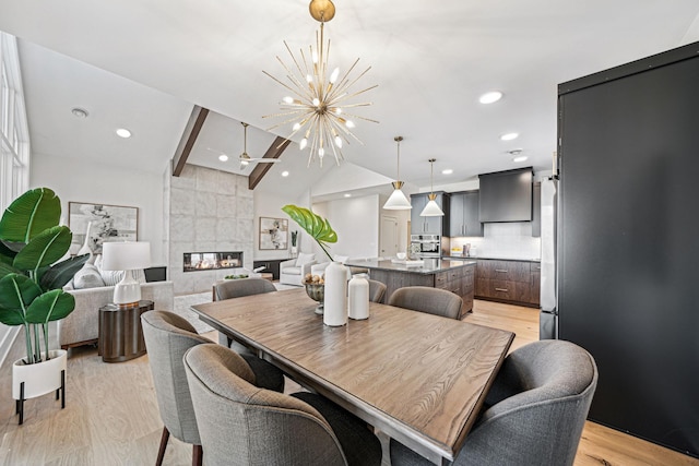 dining space featuring light wood-type flooring, vaulted ceiling, an inviting chandelier, and a fireplace