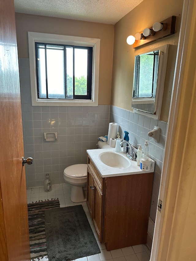 bathroom featuring a textured ceiling, tile patterned flooring, tile walls, vanity, and toilet