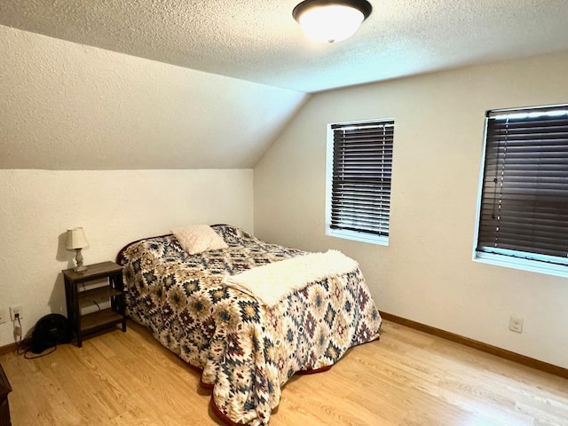 bedroom featuring a textured ceiling, light hardwood / wood-style floors, and vaulted ceiling