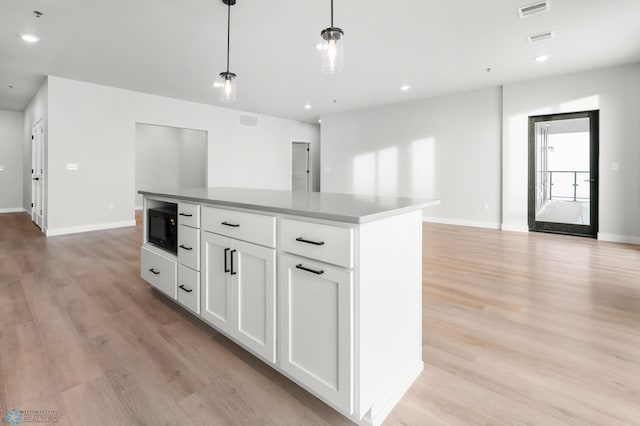 kitchen with a kitchen island, pendant lighting, black microwave, white cabinetry, and light hardwood / wood-style flooring