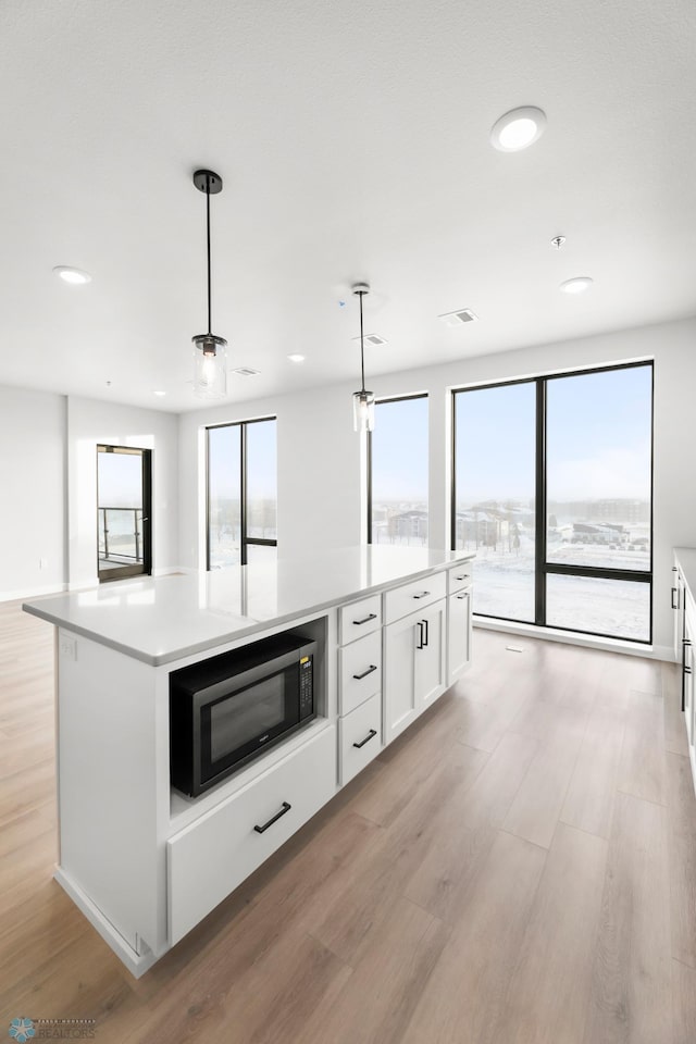 kitchen featuring white cabinetry, decorative light fixtures, a center island, and light wood-type flooring