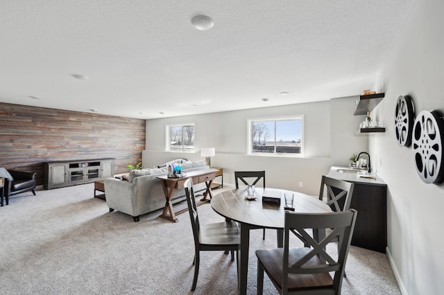 dining room with a textured ceiling, light colored carpet, sink, and wooden walls