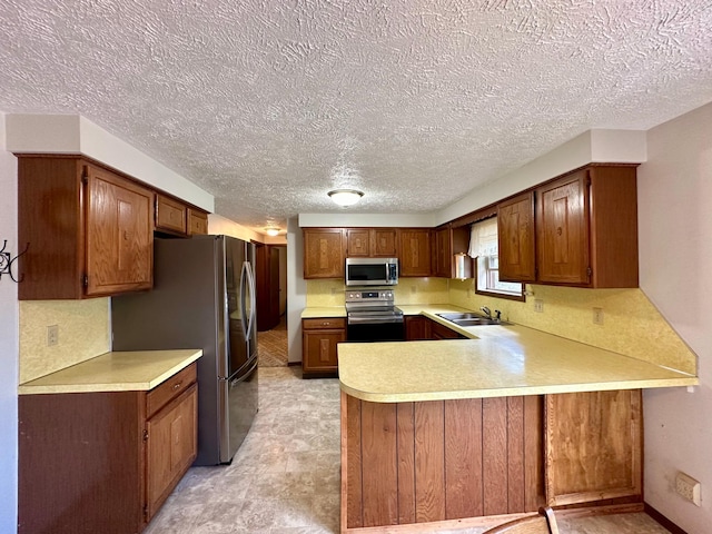 kitchen with appliances with stainless steel finishes, a textured ceiling, kitchen peninsula, and sink