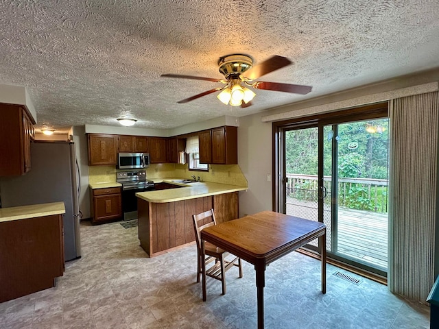 kitchen with appliances with stainless steel finishes, kitchen peninsula, a textured ceiling, ceiling fan, and sink