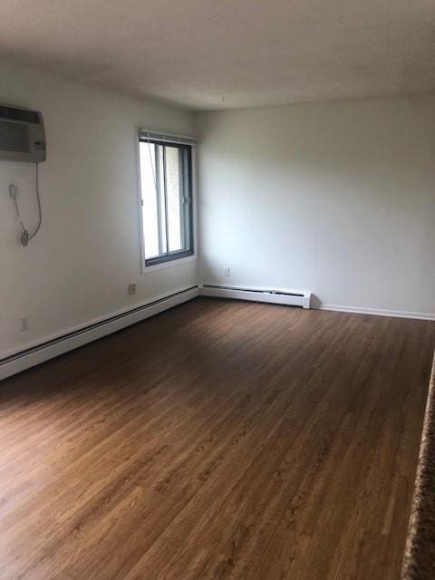 empty room featuring hardwood / wood-style floors, baseboard heating, and a wall unit AC